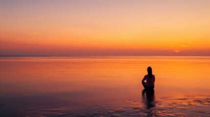 Fototapeta premium Silhouette of a woman standing in the ocean at sunset