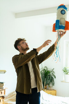 Young man with rocketship shaped pinata in bedroom at home