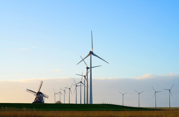 Old windmill near wind turbines under sky at sunset