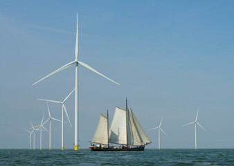 Sailboats moving in front of wind turbines in sea under sky