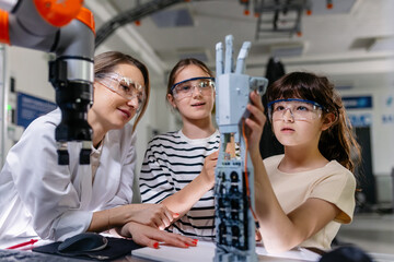 Mom and daughters during take your kid to work day, encouraging them in career in robotics. Field trip to real robotics laboratory. Real scientist talking to girls, showing prosthetic robot hand.