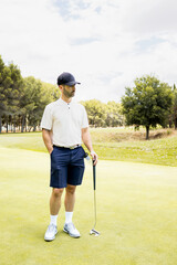 Fototapeta premium An elegant adult man plays a game of golf at a country club. The male stands watching the trajectory of the ball with one hand in his pocket. Concept of rich men playing golf.