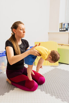Physiotherapist while rehab working with baby patient with movement and coordination disorders, testing of reflexes using Hammersmith exam
