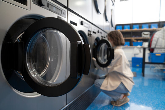 Young woman squatting near washing machines in laundromat