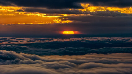 A golden sun is setting behind dark clouds in an orange sky.