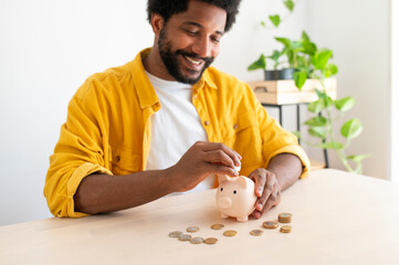 Smiling young man putting coins in piggy bank