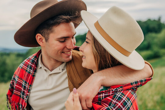 Smiling man with arm around girlfriend in plaid shawl on meadow