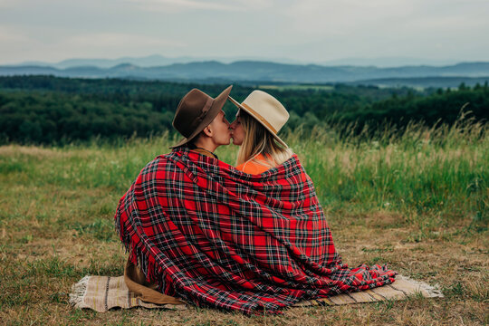 Romantic young couple in plaid shawl sitting and kissing at meadow in mountain of Poland