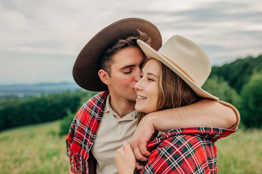 Young man kissing girlfriend wearing plaid shawl on meadow