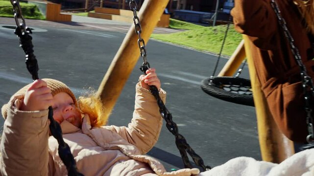 Mother And Daughter Swinging On Playground In Spring