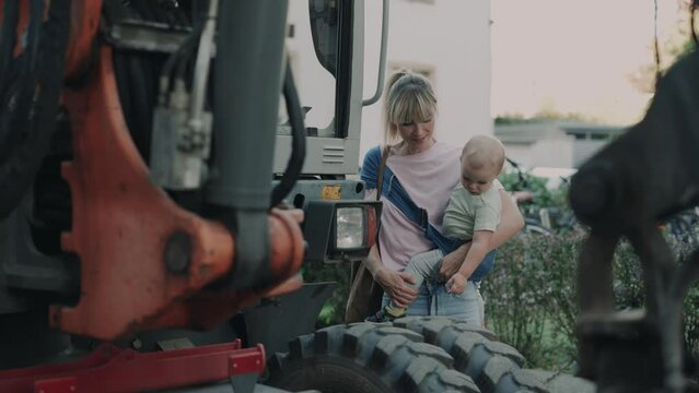 Mother pointing at construction vehicles with baby on her arm