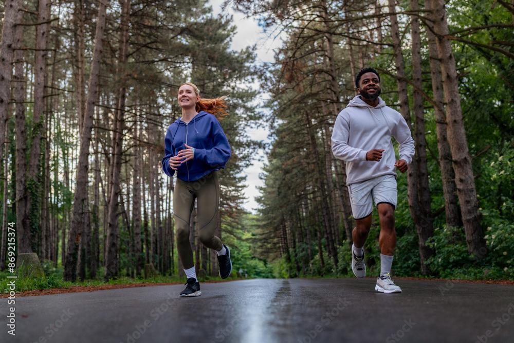 Wall mural Two friends running through a scenic forest path, sharing joy and fitness. Wearing hoodies and athletic gear, they highlight the importance of exercise and companionship. - Wall murals