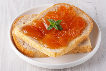 Toasted bread with apricot jam and mint on a white wooden table. Tasty breakfast