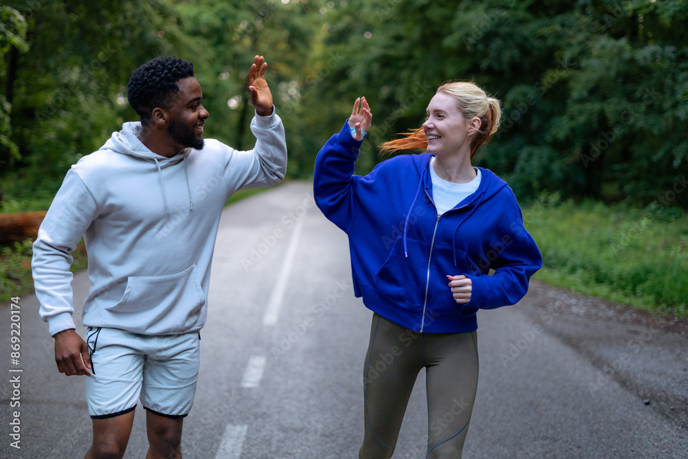 Wall mural Diverse friends giving a high five during their run in the park, smiling and enjoying their workout together. Dressed in sportswear, they celebrate their fitness journey. - Wall murals