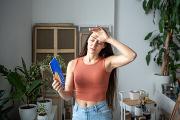 Tired woman with fan suffers from summer heat. Exhausted girl fanning, trying to cope, escape from...