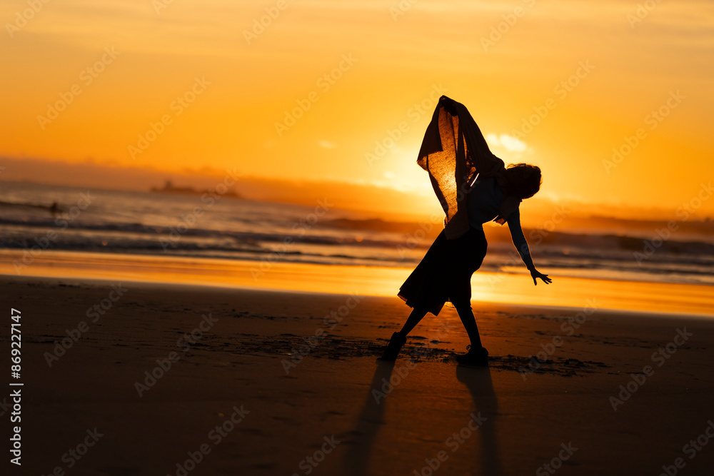 Wall mural A woman is dancing on the beach in the evening - Wall murals