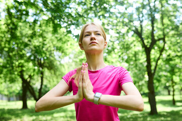 Slender blond woman performs standing meditation in the park in the morning