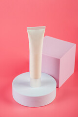 Plastic white tube for cream or lotion. Skin care or sunscreen cosmetic with stylish props on pink background.