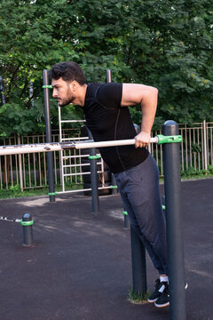A young guy is training on parallel bars in a sports park
