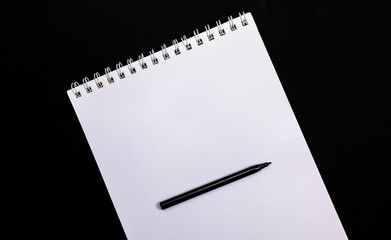 Ein schwarzer Stift liegt auf einem Ringbuch. Mit Platz für eine Notiz.