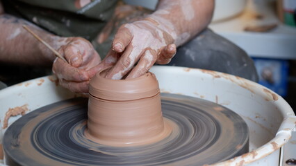 Hand cutting excess clay and smoothing pottery clay using wet foam on throwing wheel.