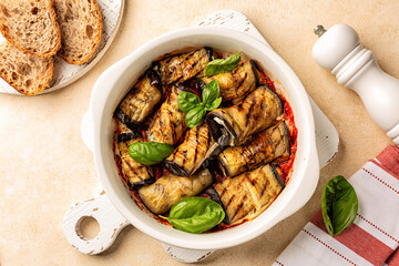 Top view of Eggplant Rollatini or rolls stuffed with ricotta cheese and baked in oven with tomato sauce in a white casserole, decorated with basil leaves.