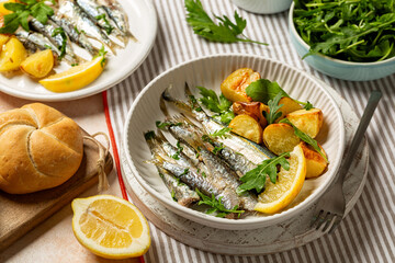 Mediterranean style dinner, sardine and baked baby potato salad with arugula. Oven baked italian fish sardoncini or sardines, with olive oil, lemon and parsley.