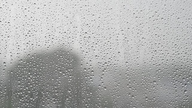 rain falling, raining outside window, focus on drops on window, summer rain in gloomy day in city