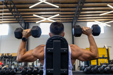 Strong man from behind, training back with dumbbells sitting