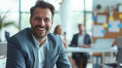 Fototapeta premium Young business office employee sitting in office smiling and looking at camera with office colleagues on blur background