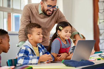 Primary students using laptop with male teacher