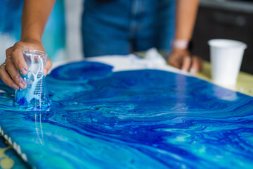 Person creating blue acrylic pour art on canvas. Art and creativity concept.