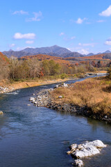 Fototapeta premium 北海道平取町、紅葉した木々の合間を流れる沙流川と日高山脈【11月】