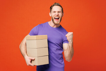 Young excited cool fun happy man he wearing purple t-shirt casual clothes holding stack cardboard blank boxes doing winner gesture isolated on red orange background studio portrait. Lifestyle concept.