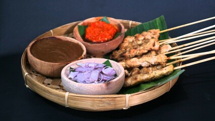 Chicken satay with peanut sauce, chili sauce, and sliced onion, indonesian skewer cuisine, served on wooden plate, isolated white