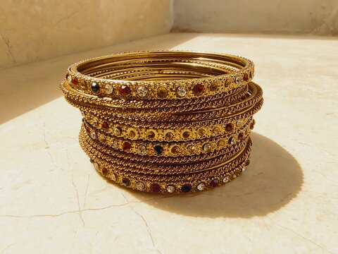 A set of metallic golden color bangles isolated background in sunlight, wedding female round rings golden brown collection bangles jewelry with gem stones photography