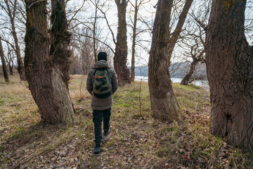 A teenage boy walking along the riverbank and forest, early spring landscape, the concept of hiking and outdoor activities