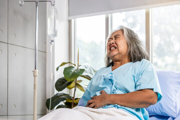 Asian elderly woman has a stomachache, severe abdominal pain, She sat on the bed, The concept of health care for the elderly. Illness. Health insurance, problems with liver disease, colorectal cancer