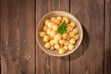 Cooked chickpeas in a ceramic bowl on a rustic wooden table decorated with a parsley leaf, ready to eat