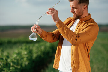 Scientific research, with test tube. Handsome man is on the agricultural field at daytime