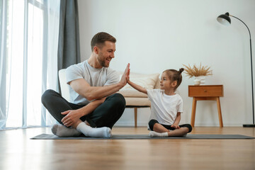 Father with little daughter are doing yoga at home