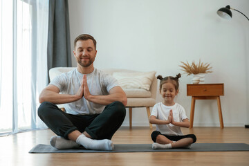 Fototapeta premium Father with little daughter are doing yoga at home