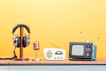 Old TV, radio, microphone and headphones front yellow background. Retro style filtered photo