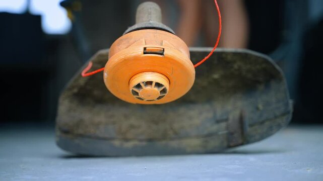Unsuccessful attempts to start the engine of a gasoline trimmer. A man in the background pulls the recoil starter of a two-stroke engine to no avail.