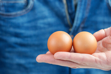 Two eggs held in a hand, with blue jeans in the background.