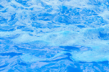 Soft white foam on blue water ripples close up