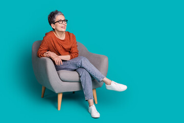 Full length photo of lovely pensioner lady sit armchair look empty space dressed stylish brown garment isolated on cyan color background