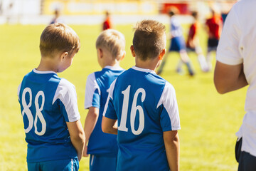 Football players wearing white jersey shirts in the youth team. Boys in blue jersey shirts watching...