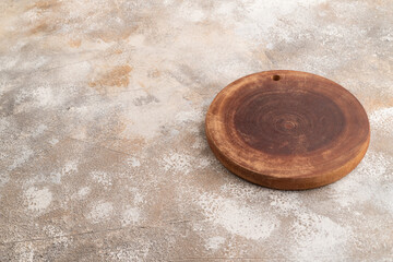 Empty round wooden cutting board on brown concrete. Side view, copy space