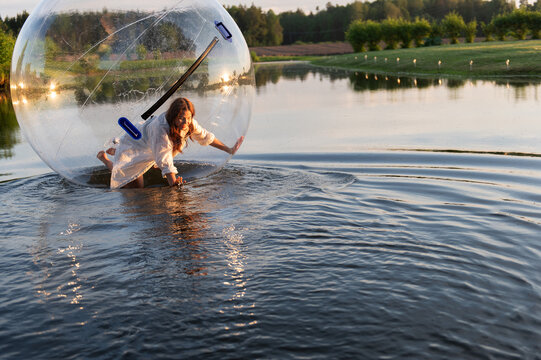 Water ball (similar to zorb or Human Hamster Ball) with young woman inside on pond surface